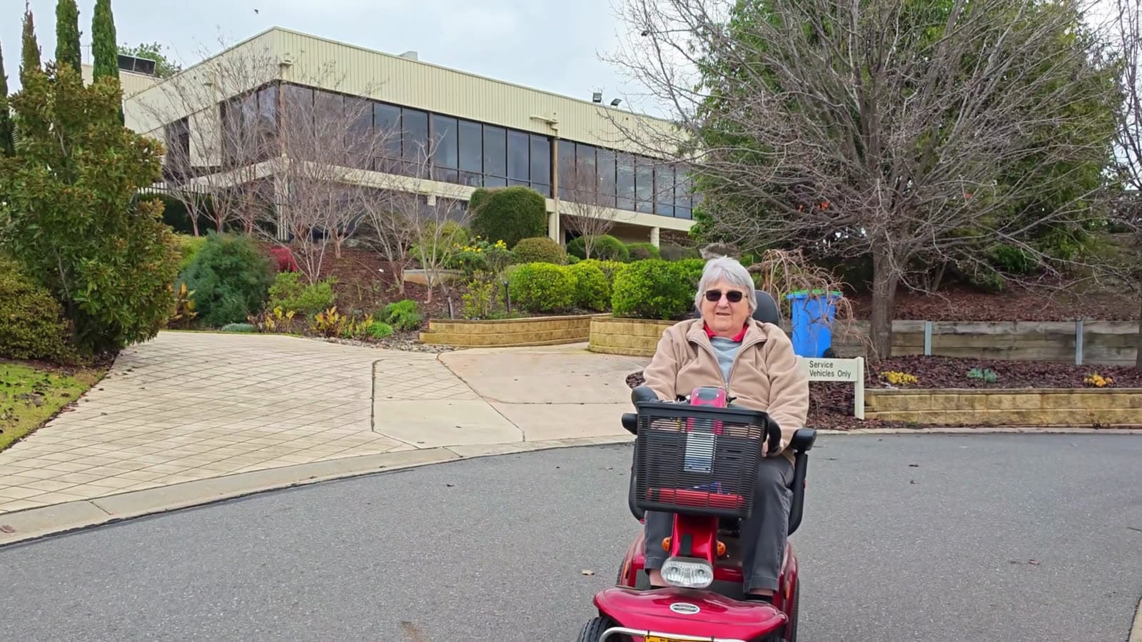 A woman riding a mobility scooter along a residential driveway
