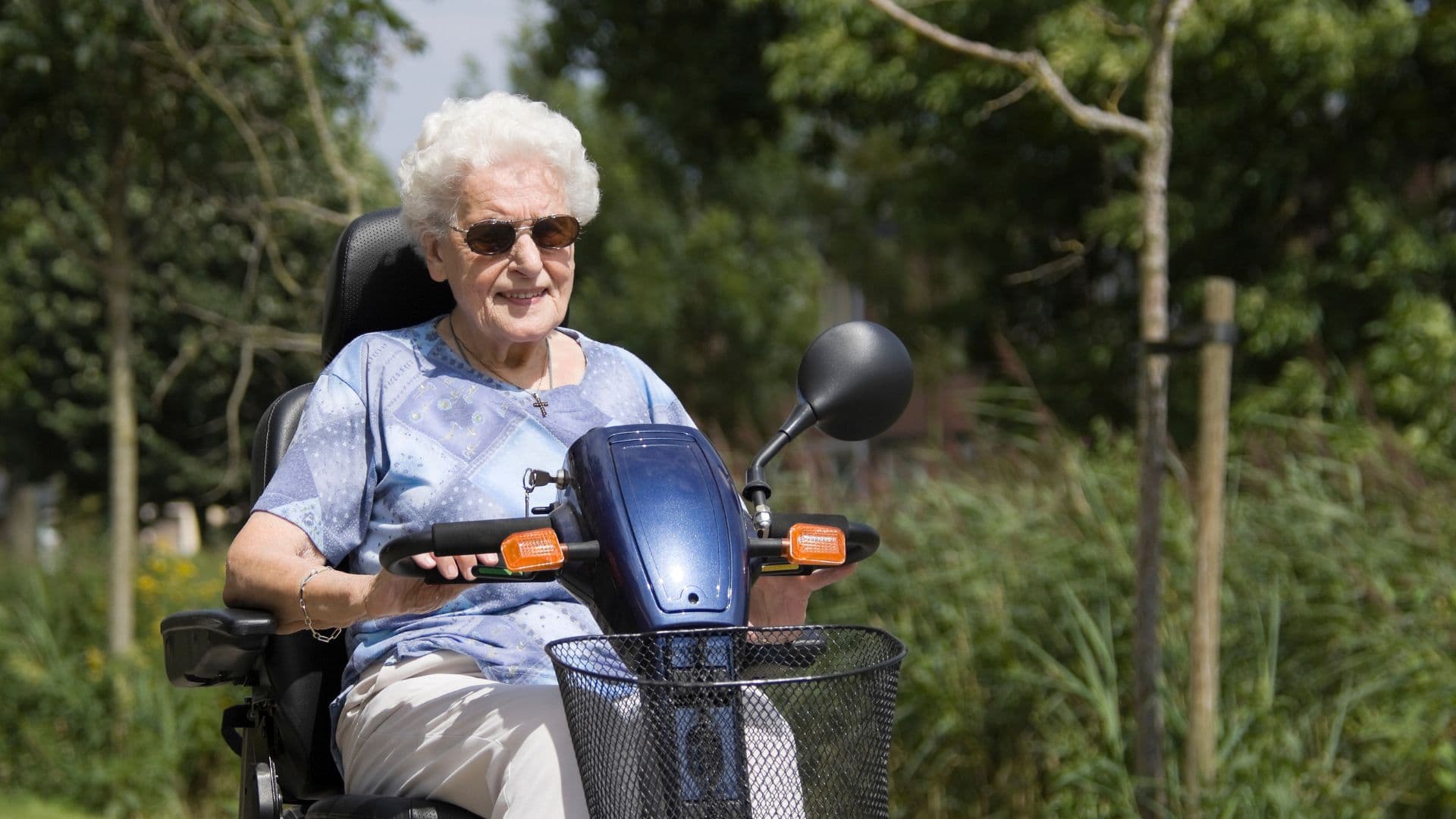 A woman sitting on a mobility scooter on a path through a sunlit park