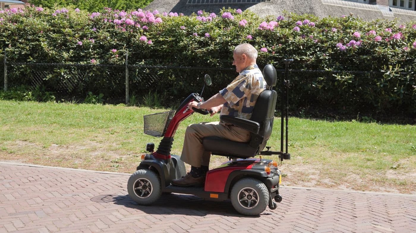 A man riding a road-class mobility scooter along a brick path