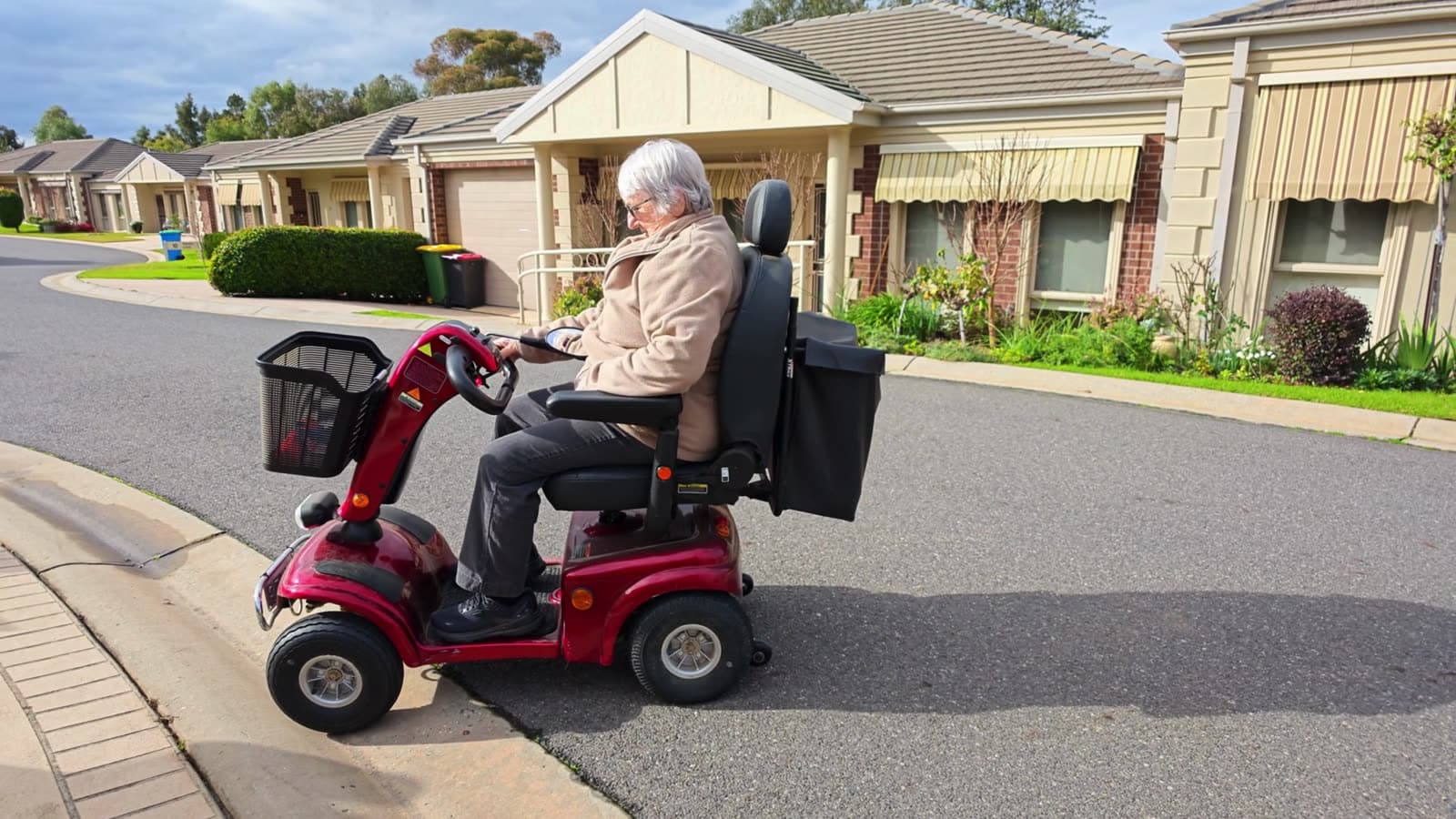 A woman getting onto her mobility scooter outside her home and setting off along the road