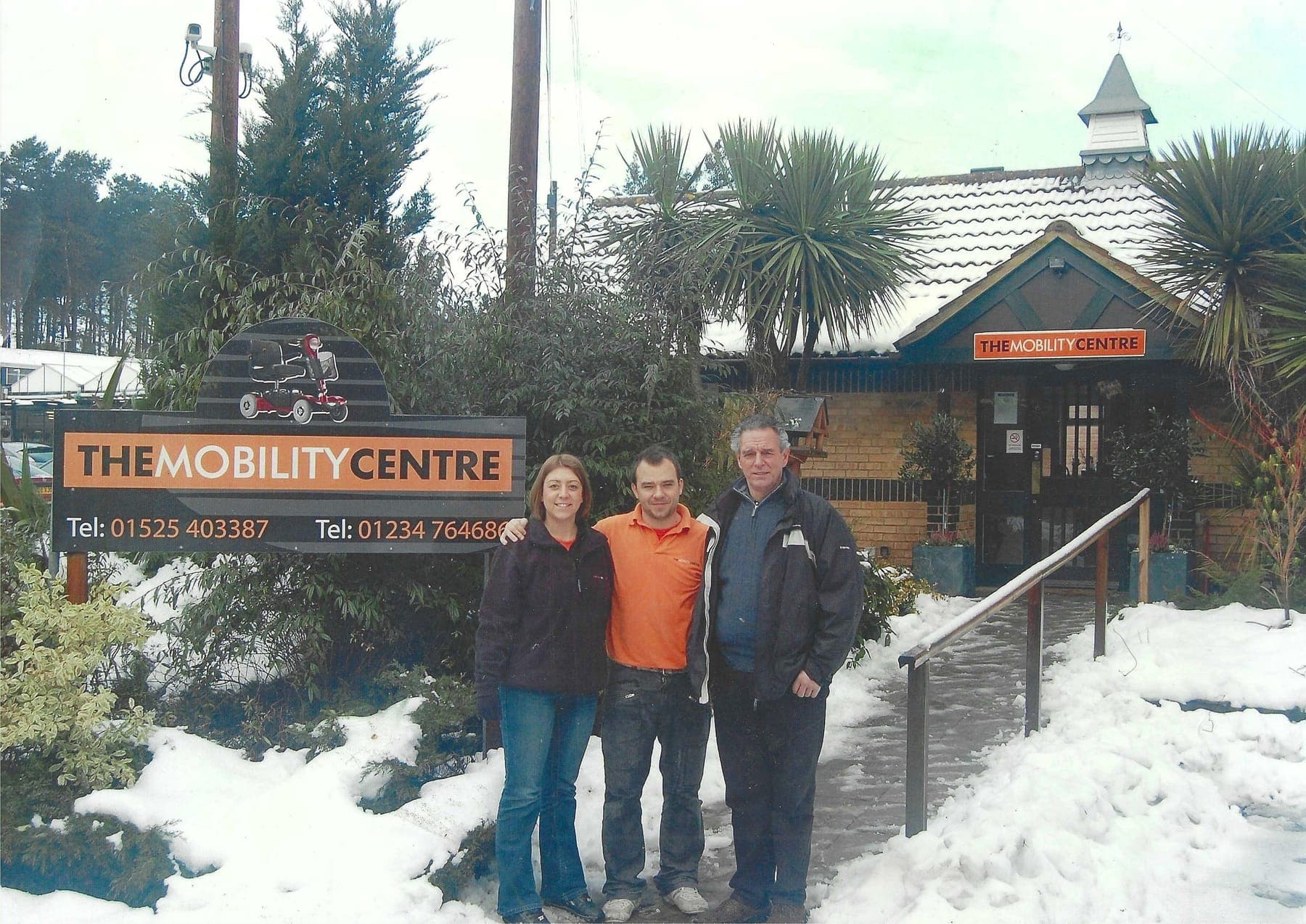 The team in the early days, standing in the snow outside The Mobility Centre with its orange sign